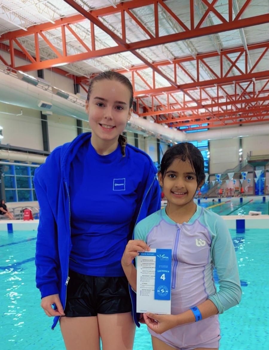 Unnati Raj poolside holding her Swimmer 4 report card beside her instructor
